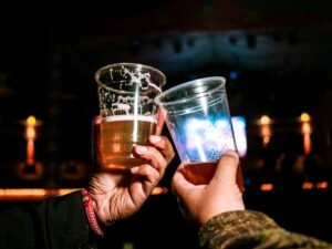 Two people clinking plastic beer cups at a lively nighttime party setting.
