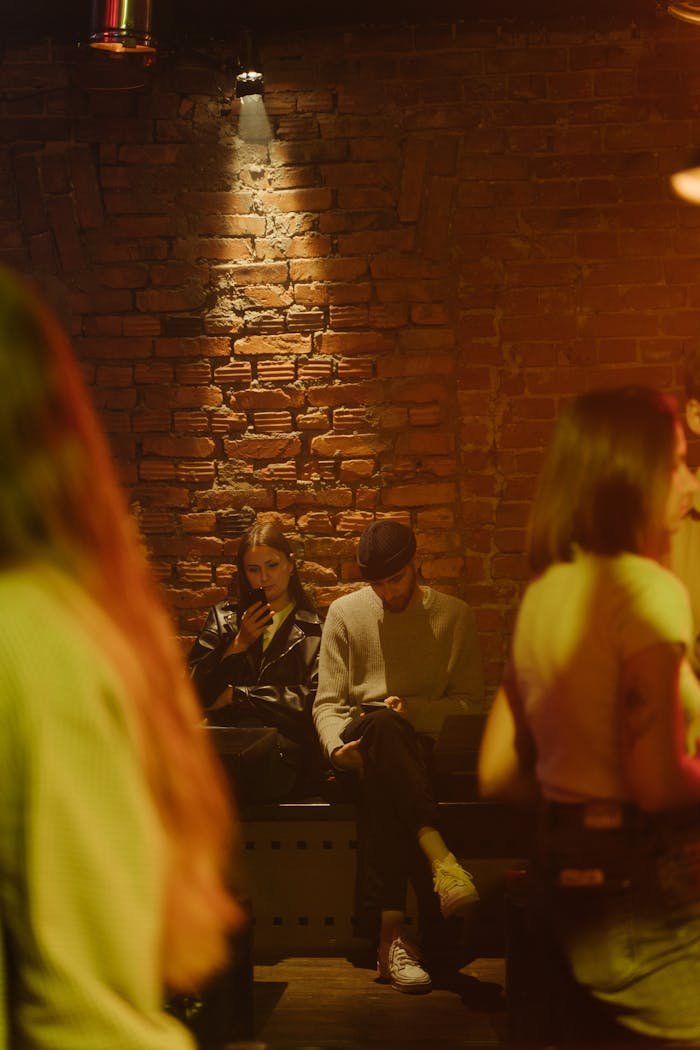 Warm lit bar featuring a relaxed couple sitting, engaging with their phones amidst nightlife.